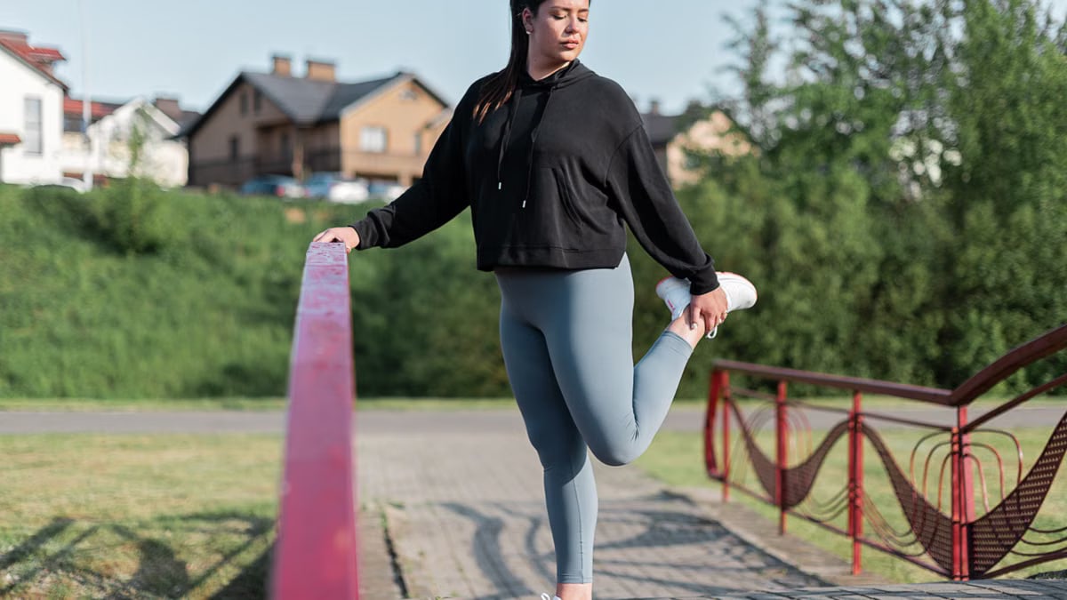 Young woman in activewear stretching on a red railing outdoors.