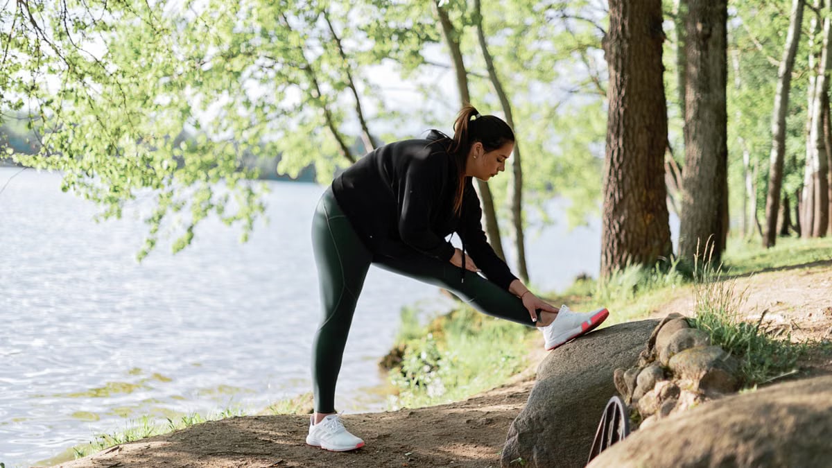 A woman in sportswear stretches by a serene lake surrounded by trees, embracing nature and fitness.